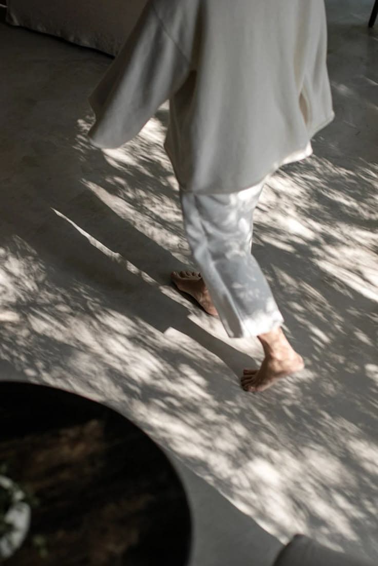 Walking barefoot through tree shadow in wide-legged trousers